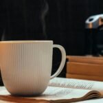 A steaming coffee mug rests on an open book, creating a cozy reading nook ambiance.