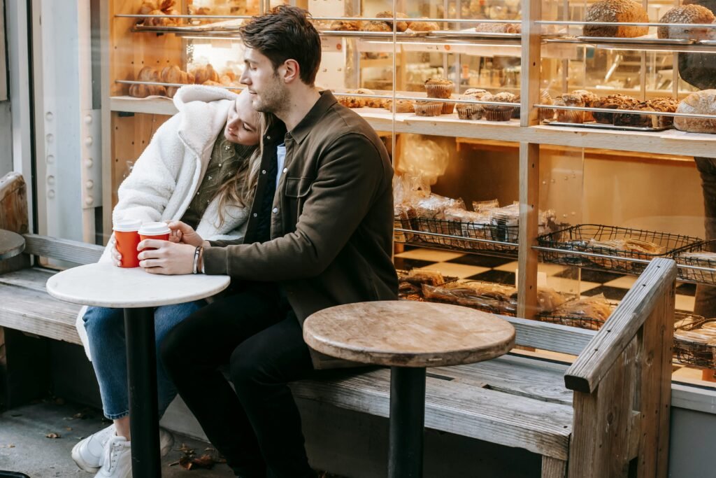 A couple enjoys a relaxing moment with coffee outside a cozy bakery, capturing warmth and affection.