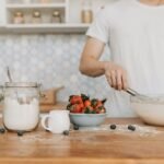 A man in a white shirt prepares batter with strawberries and blueberries on a kitchen counter.