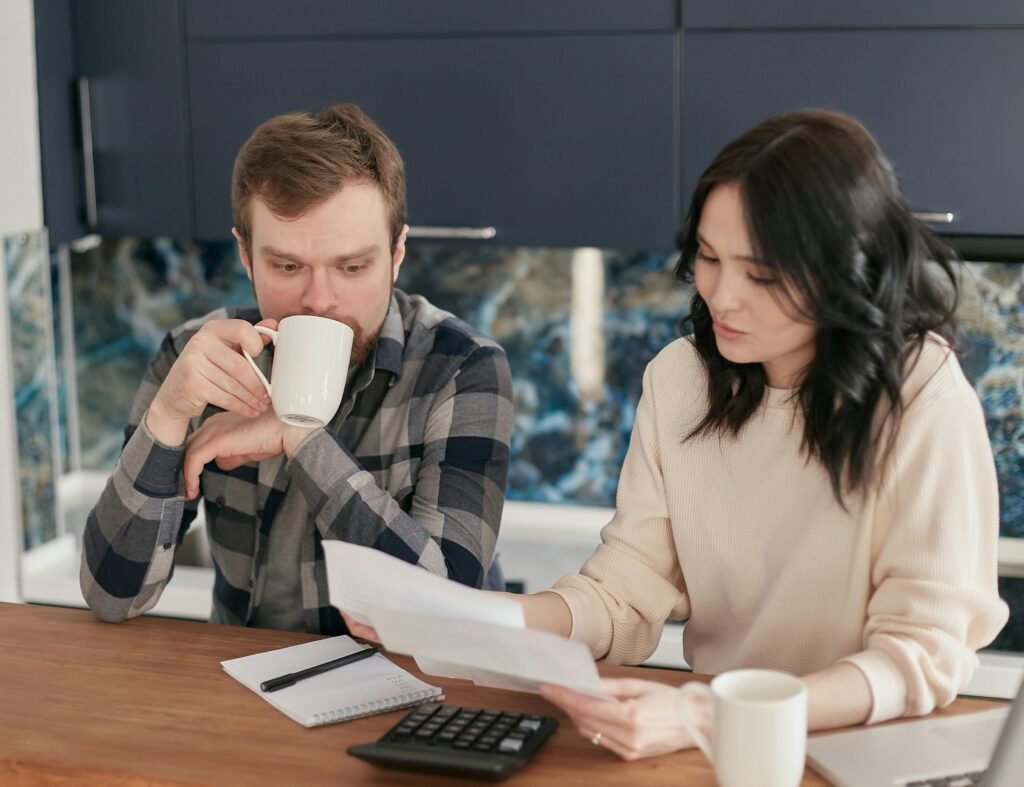 A couple reviewing bills using a calculator and paperwork, symbolizing financial planning at home.