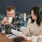 A couple reviewing bills using a calculator and paperwork, symbolizing financial planning at home.