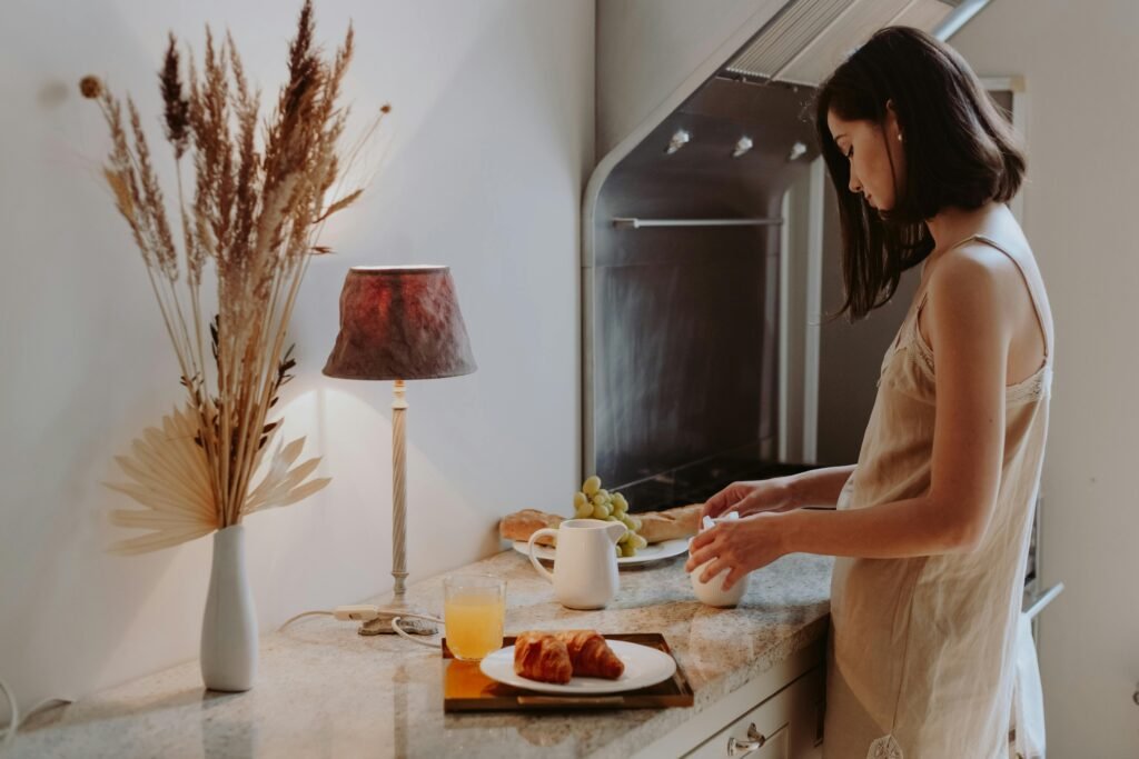 A young woman prepares breakfast in a cozy kitchen with croissants and juice.